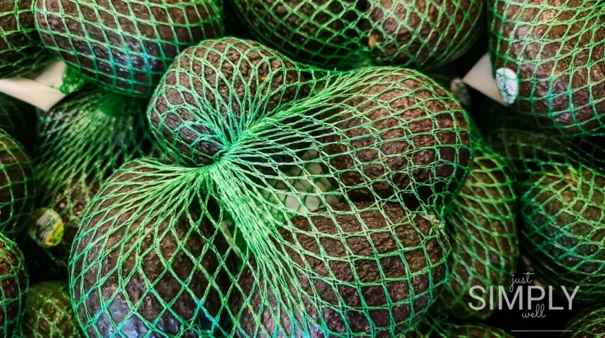 Close-up of Haas avocados in green netting at a grocery store.